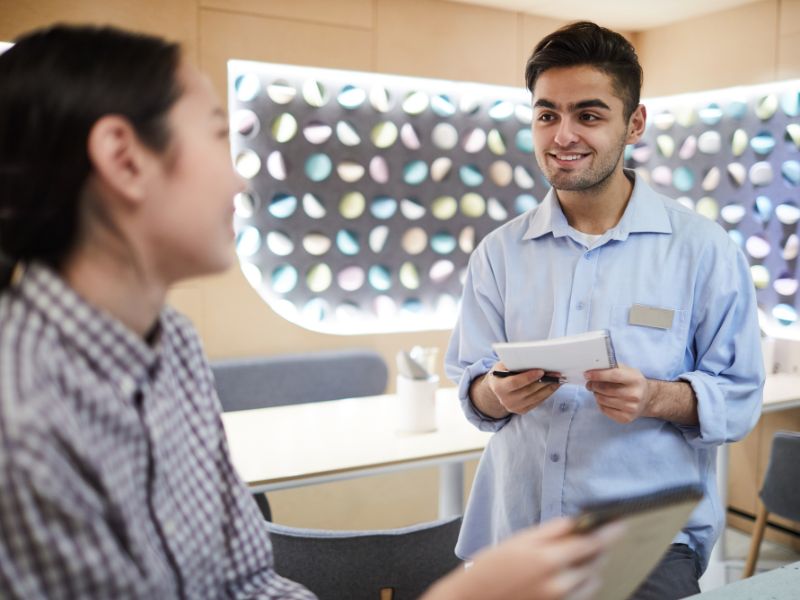 Retail employee with a name badge helping a customer choose eyewear in a modern store